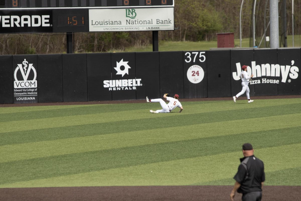 ULM baseball Outfielder #5 Davis Mauzy sliding in outfield to catch a pop fly.